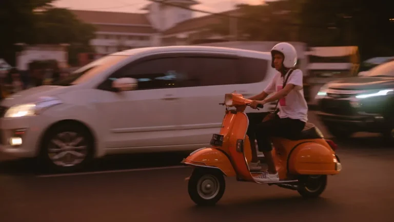 a person riding vespa next to a white car