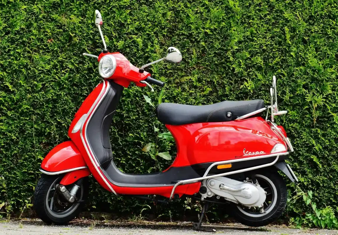 red vespa standing near a bush